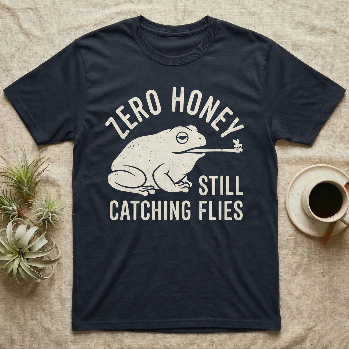 Tree Frog Proverb T-Shirt in Navy — Worn cream print of a dumpy White's tree frog catching a fly with its tongue under the words Zero Honey, Still Catching Flies