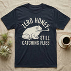 Tree Frog Proverb T-Shirt in Navy — Worn cream print of a dumpy White's tree frog catching a fly with its tongue under the words Zero Honey, Still Catching Flies