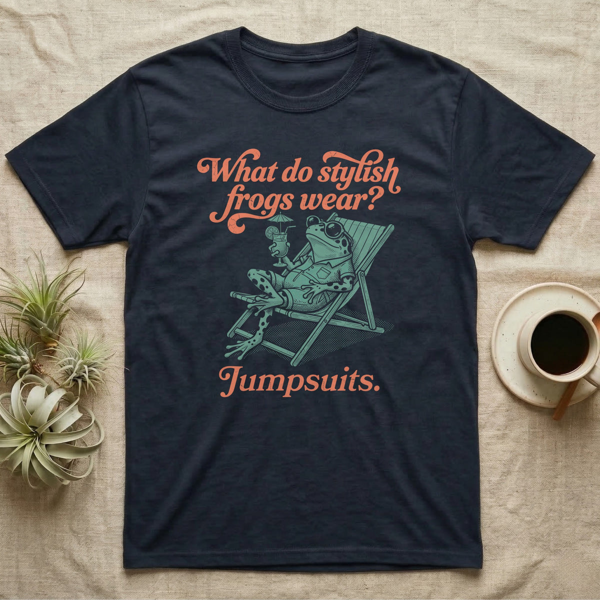 Poison Dart Frog Jumpsuit T-Shirt in Navy — Illustrated green and black poison dart frog reclining in a beach chair with sunglasses and a cocktail, coral script asking what stylish frogs wear, answer jumpsuits.