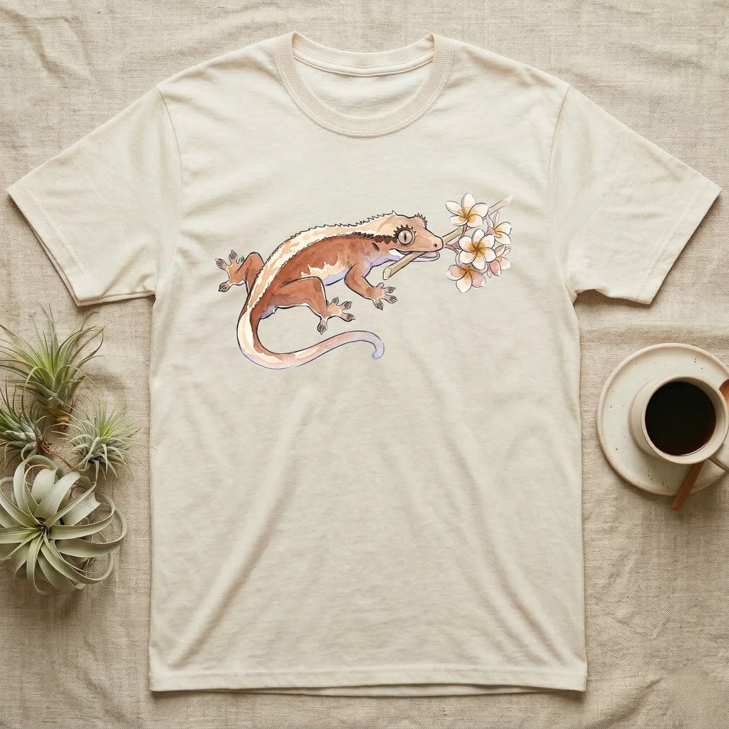 Crested Gecko Blossom T-Shirt in Natural — Watercolor illustration of a rust-brown crested gecko holding a frangipani blossom sprig, on a dark grey t-shirt.