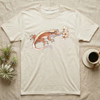 Crested Gecko Blossom T-Shirt in Natural — Watercolor illustration of a rust-brown crested gecko holding a frangipani blossom sprig, on a dark grey t-shirt.