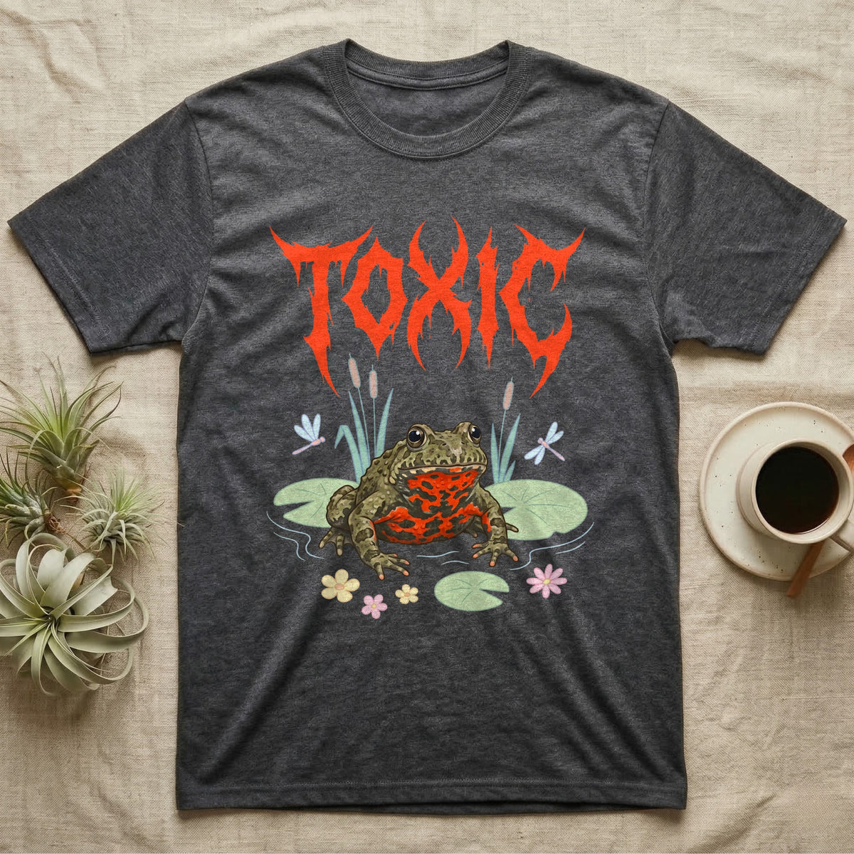 Oriental Fire-Bellied Toad Feral T-Shirt in Dark Heather — Pastel fire-bellied toad with red-orange belly among lily pads and dragonflies, jagged metal wordmark "TOXIC" above.