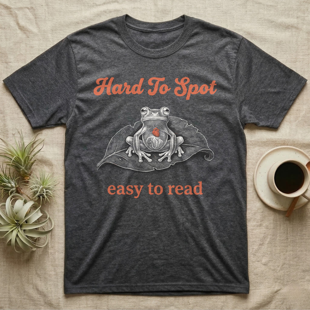 Glass Frog Engraving T-Shirt in Dark Heather — White-line engraving of a glass frog sitting on a leaf with a coral heart showing through its belly, between Hard To Spot and easy to read