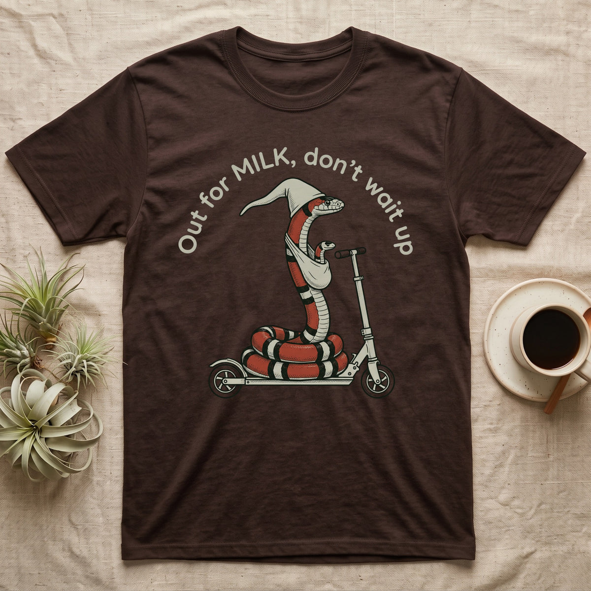Milk Snake Scooter T-Shirt in Dark Chocolate — Milk snake in a white cap riding a kick scooter with a baby snake in a sling, under the curved words Out for MILK, don't wait up.