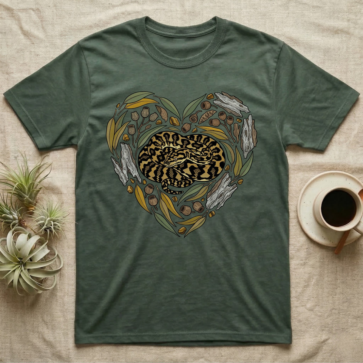 Green t-shirt with heart-shaped graphic of a coiled snake surrounded by eucalyptus leaves and acorns.