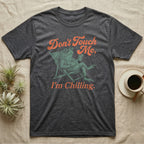 American Toad Deck Chair T-Shirt in Dark Heather — Illustrated American toad reclining in a deck chair with sunglasses and a drink, coral script reading Don't Touch Me I'm Chilling.