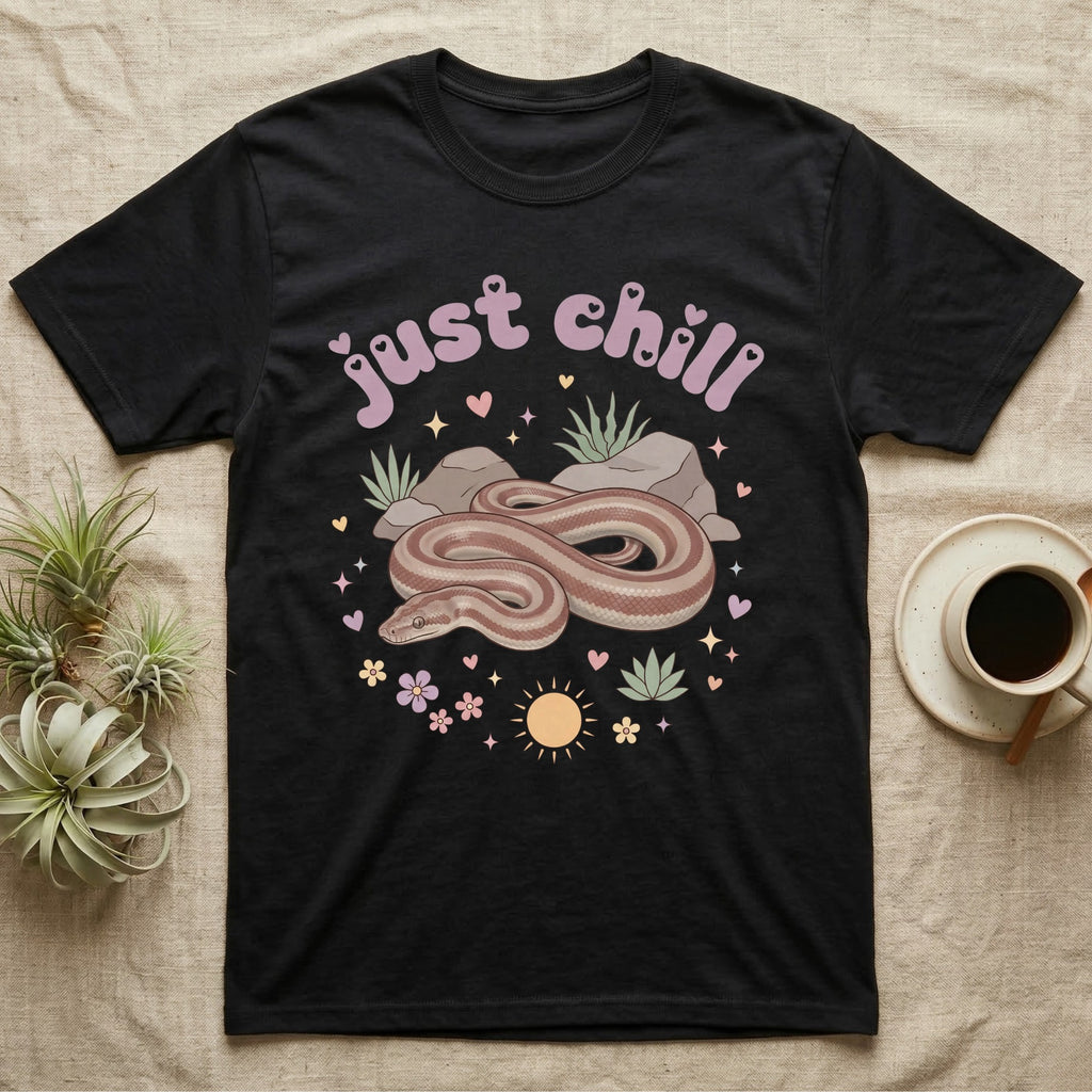 Rosy Boa Softie T-Shirt in Black — Relaxed coiled rosy boa with sleepy eyes under pastel bubble text "just chill" with tiny hearts.