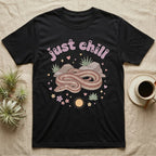 Rosy Boa Softie T-Shirt in Black — Relaxed coiled rosy boa with sleepy eyes under pastel bubble text "just chill" with tiny hearts.