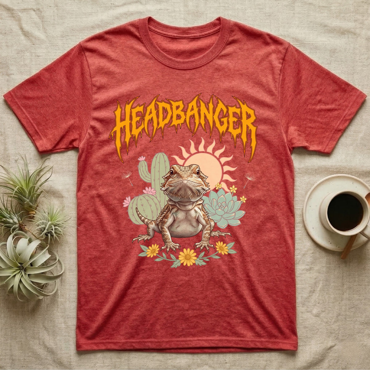 Central Bearded Dragon Feral T-Shirt in Heather Red — Baby bearded dragon in a pastel desert scene under a spiky amber metal wordmark reading HEADBANGER.