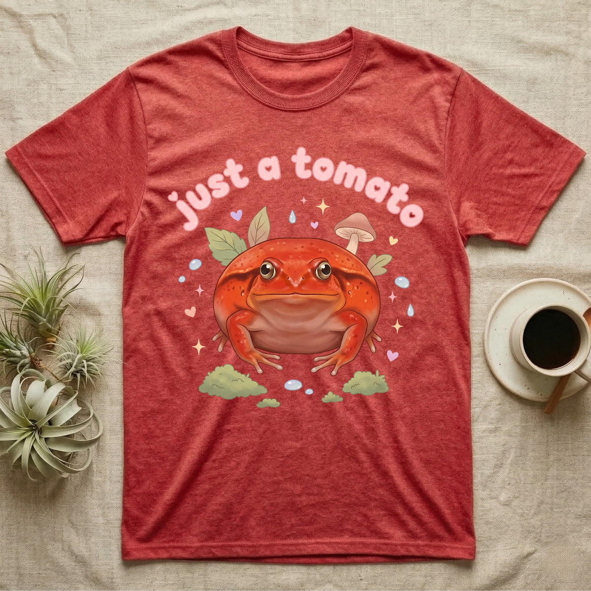 Tomato Frog Softie T-Shirt in Heather Red — Round red-orange tomato frog facing forward under a puffy pastel "just a tomato" bubble wordmark with tiny hearts.