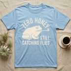 Tree Frog Proverb T-Shirt in Light Blue — Worn cream print of a dumpy White's tree frog catching a fly with its tongue under the words Zero Honey, Still Catching Flies