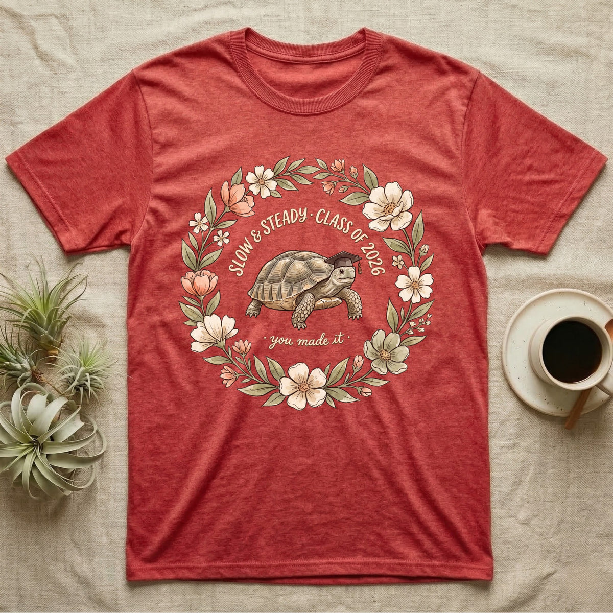Slow And Steady Graduation T-Shirt in Heather Red — Watercolour illustration of a tortoise in a graduation cap inside a floral wreath with "Slow & Steady, Class of 2026."