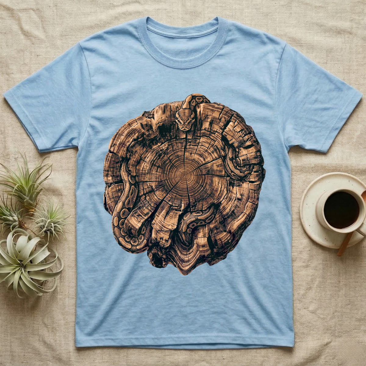 Ball Python Stump Coil T-Shirt in Light Blue — Pyrography-style illustration of a ball python threaded through the charred radial cracks of a cross-section log, no on-shirt text.