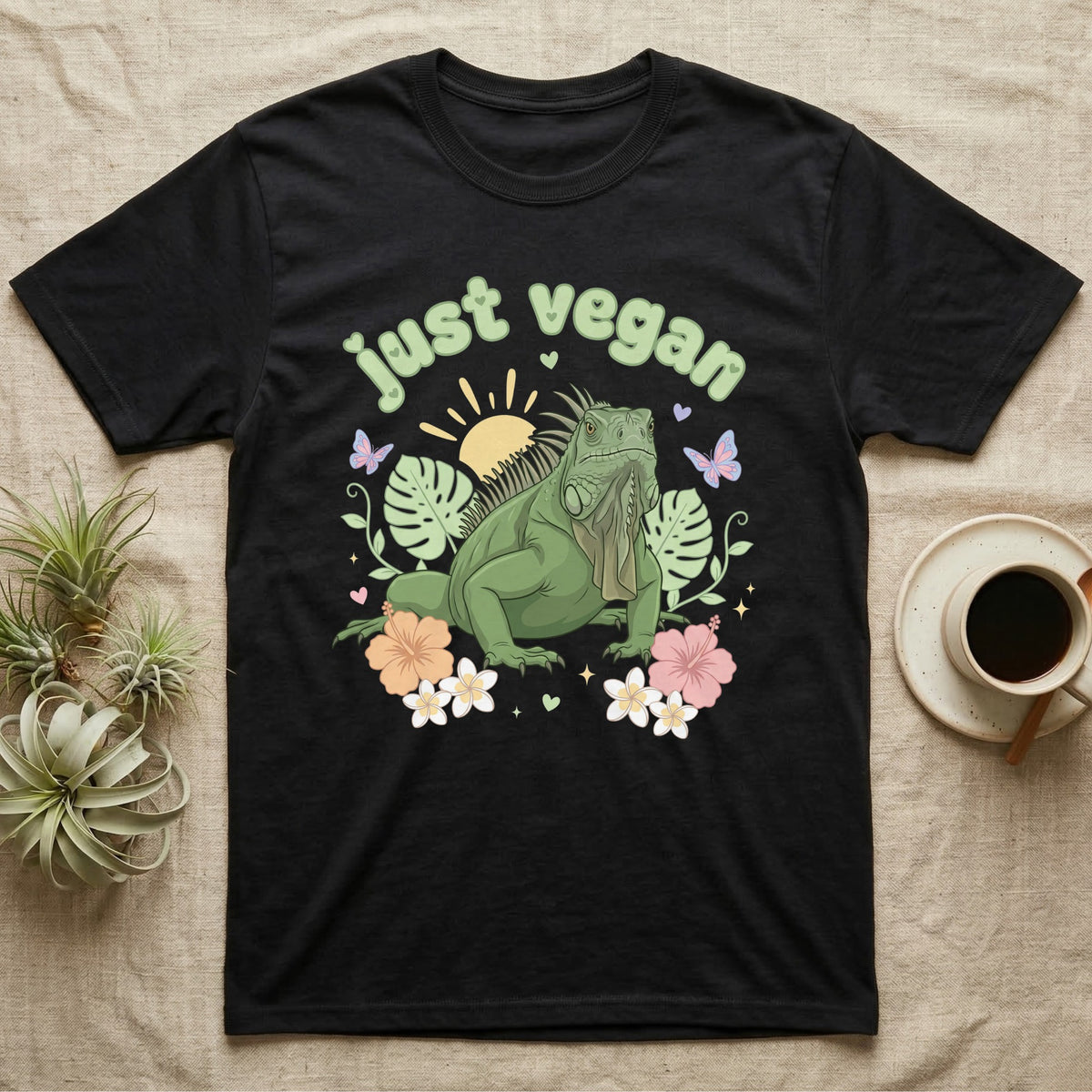 Green Iguana Baby T-Shirt in Black — Green iguana with spiky crest and dewlap among pastel leaves and flowers under puffy green bubble text "just vegan".