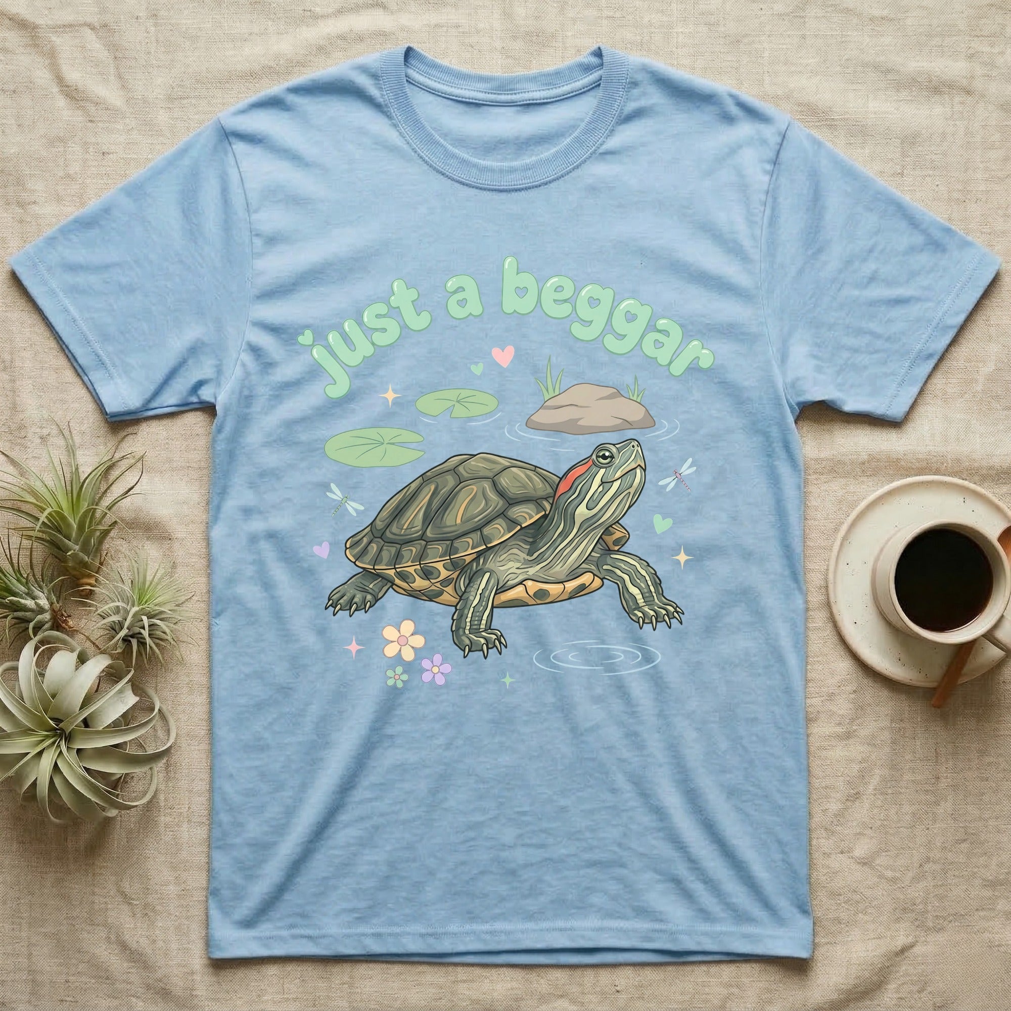 Red-Eared Slider Softie T-Shirt in Light Blue — Red-eared slider turtle stretching its neck to beg, under pastel bubble text "just a beggar" with hearts.