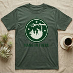 Green t-shirt with a raccoon hanging upside down in a circle logo that says "HANG IN THERE".