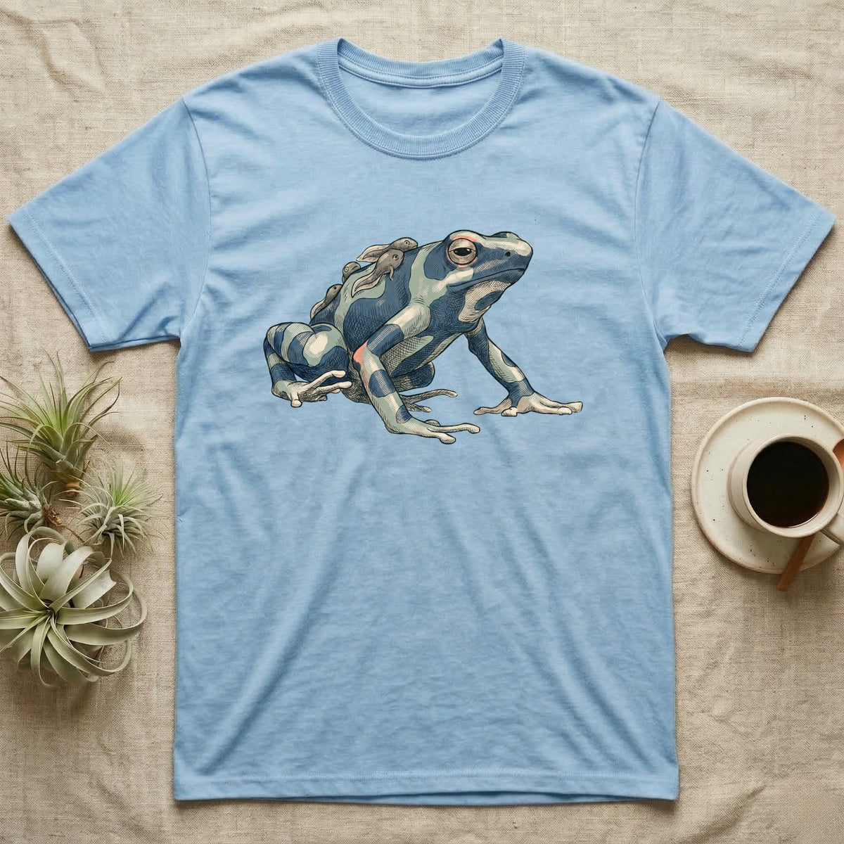 Dart Frog Tadpole T-Shirt in Light Blue — Naturalist-plate illustration of a dyeing dart frog carrying tadpoles on its back with a dry typewriter caption beside it.