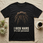Deadpan photographic mugshot of a curly hair tarantula facing the camera above the distressed text I Kick Hairs, it's not personal. — shown on a Black tee.
