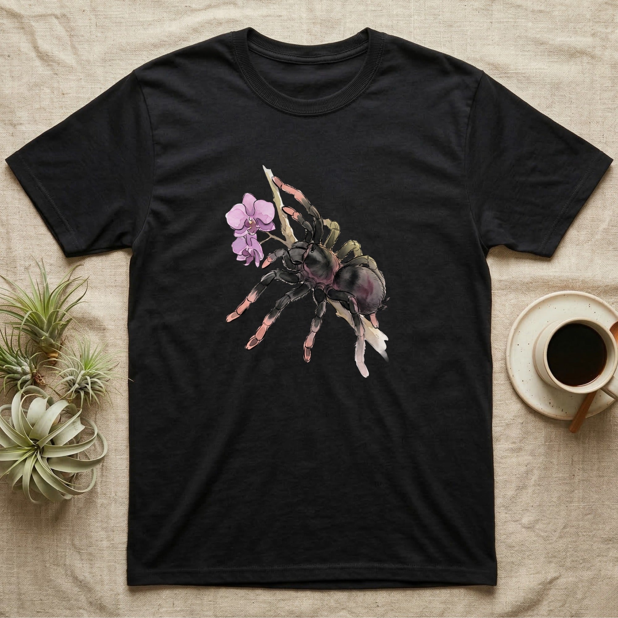 Pink-Toe Tarantula Blossom T-Shirt in Black — Watercolor illustration of a charcoal pink-toe tarantula with salmon toe tips holding an orchid blossom sprig, on a dark grey t-shirt.