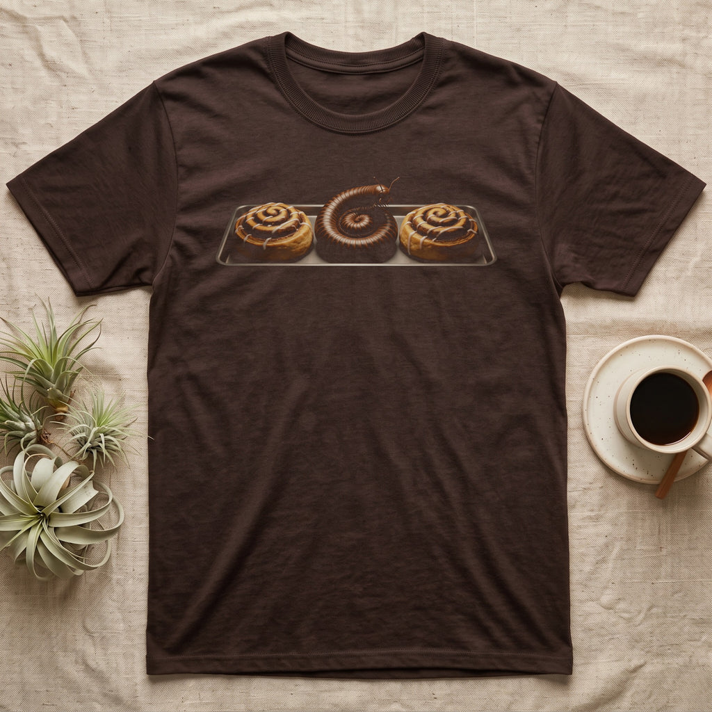Millipede Cinnamon Roll T-Shirt in Dark Chocolate — A giant African millipede curled like a cinnamon roll on a bakery tray between two iced cinnamon rolls, head raised, on black.
