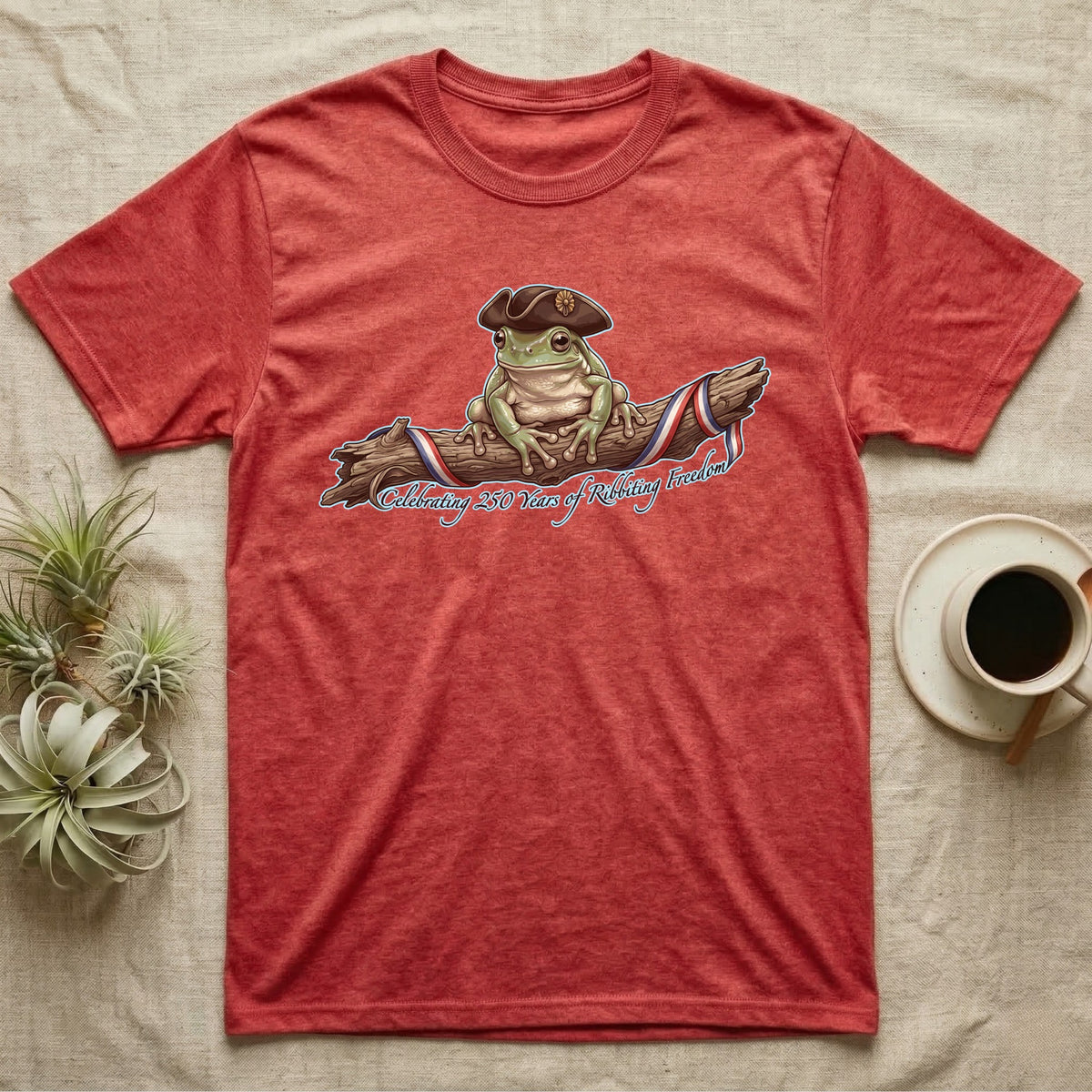 Tree Frog Freedom T-Shirt in Heather Red — Detailed green tree frog in a tricorn hat on a ribboned branch under script Celebrating 250 Years of Freedom.