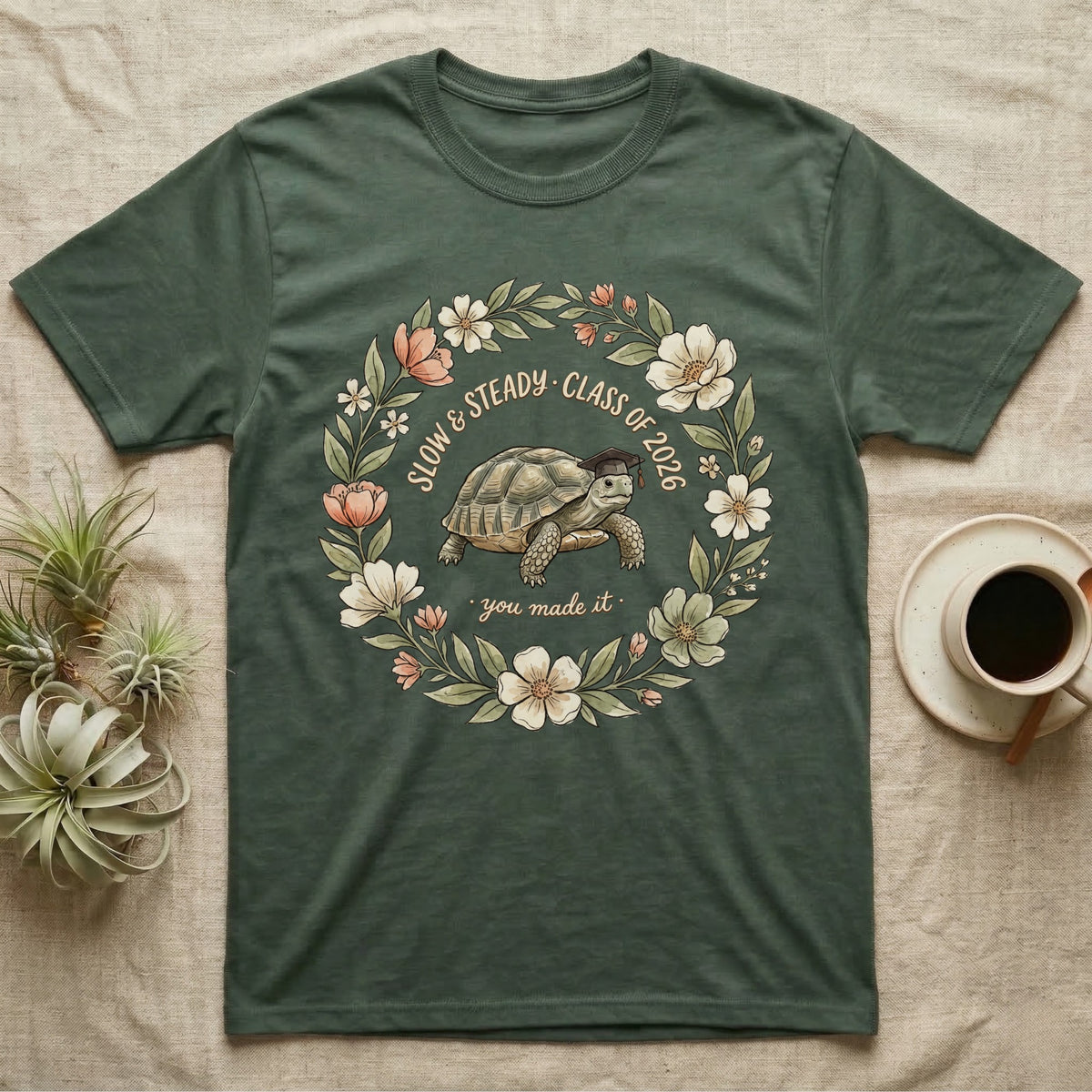 Slow And Steady Graduation T-Shirt in Military Green — Watercolour illustration of a tortoise in a graduation cap inside a floral wreath with "Slow & Steady, Class of 2026."