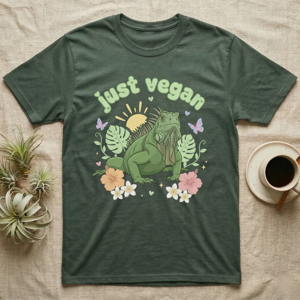 Green Iguana Baby T-Shirt in Military Green — Green iguana with spiky crest and dewlap among pastel leaves and flowers under puffy green bubble text "just vegan".