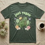 Green Iguana Baby T-Shirt in Military Green — Green iguana with spiky crest and dewlap among pastel leaves and flowers under puffy green bubble text "just vegan".