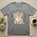 Two foxes sit in a circular arrangement of branches and leaves on a grey t-shirt.