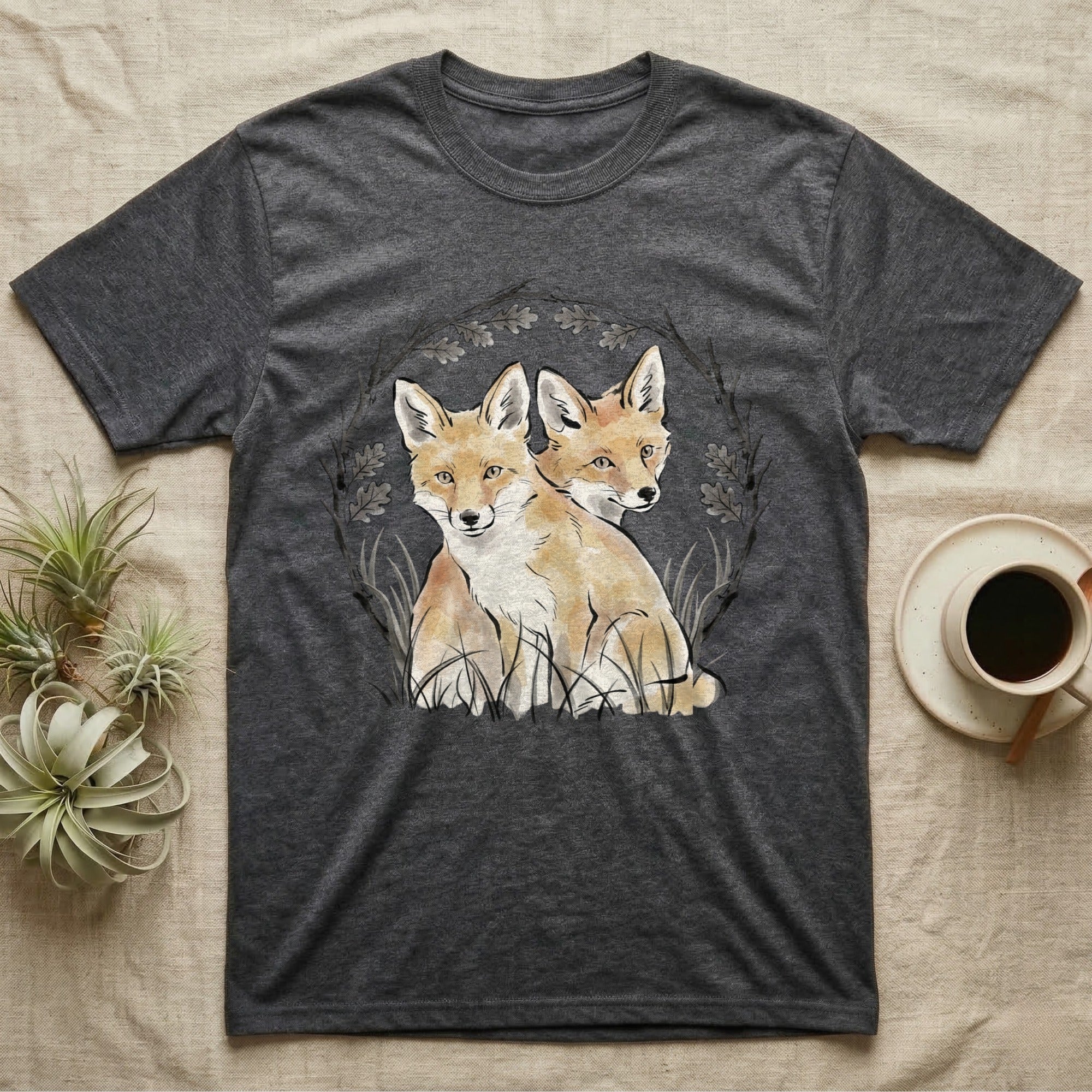 Dark grey t-shirt with illustration of two foxes in a circular wreath of branches.