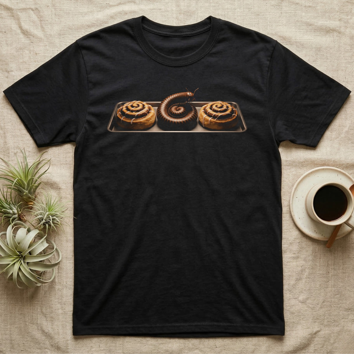 Millipede Cinnamon Roll T-Shirt in Black — A giant African millipede curled like a cinnamon roll on a bakery tray between two iced cinnamon rolls, head raised, on black.