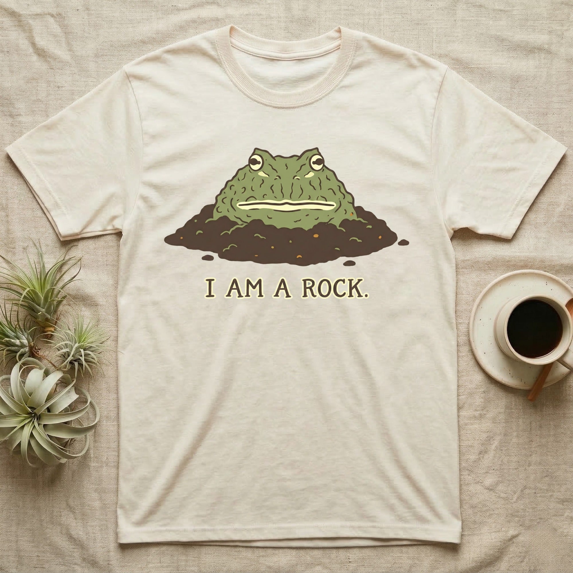 Cream t-shirt with a cartoon frog emerging from dirt, text reads "I AM A ROCK."