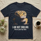 Photographic mugshot of a leopard gecko braced low and staring into the lens above the hook I Am Not Smiling, this is just my face. — shown on a Navy tee.