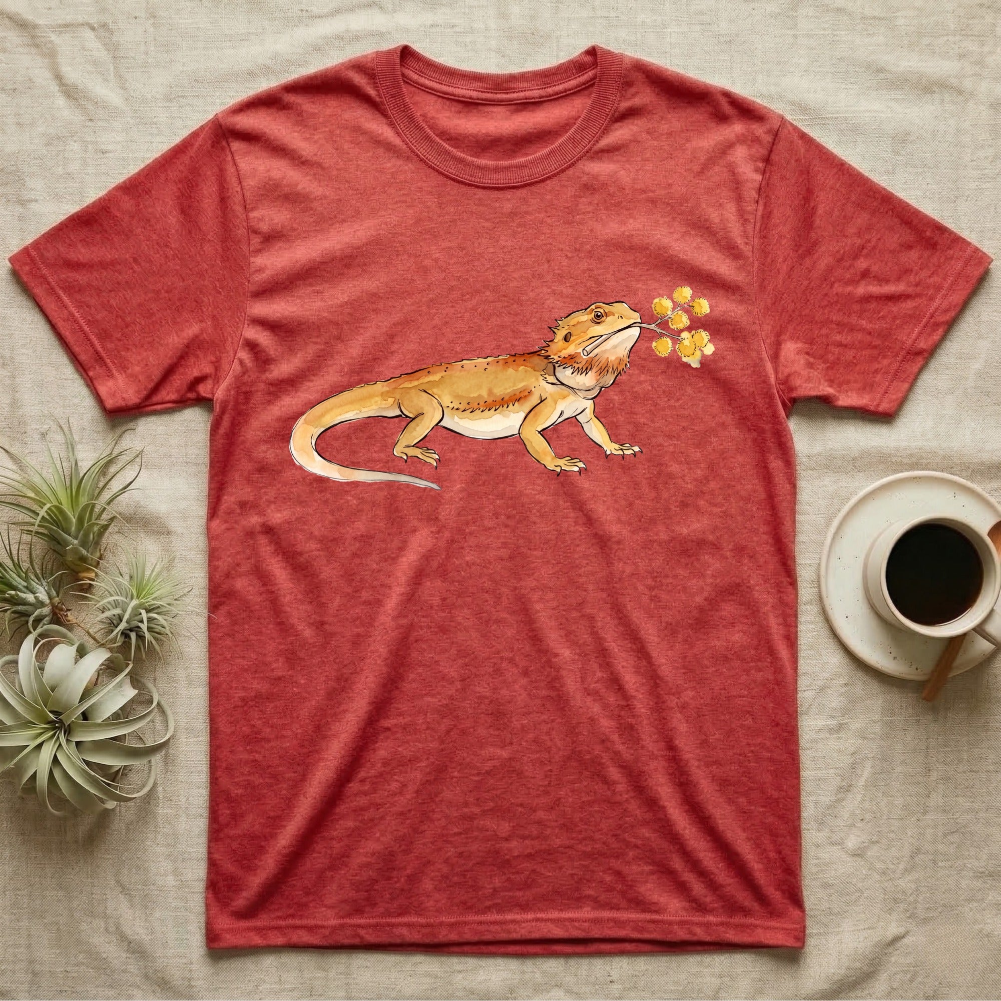 Bearded Dragon Blossom T-Shirt in Heather Red — Watercolor illustration of an ochre bearded dragon holding a golden wattle blossom sprig, on a dark grey t-shirt.