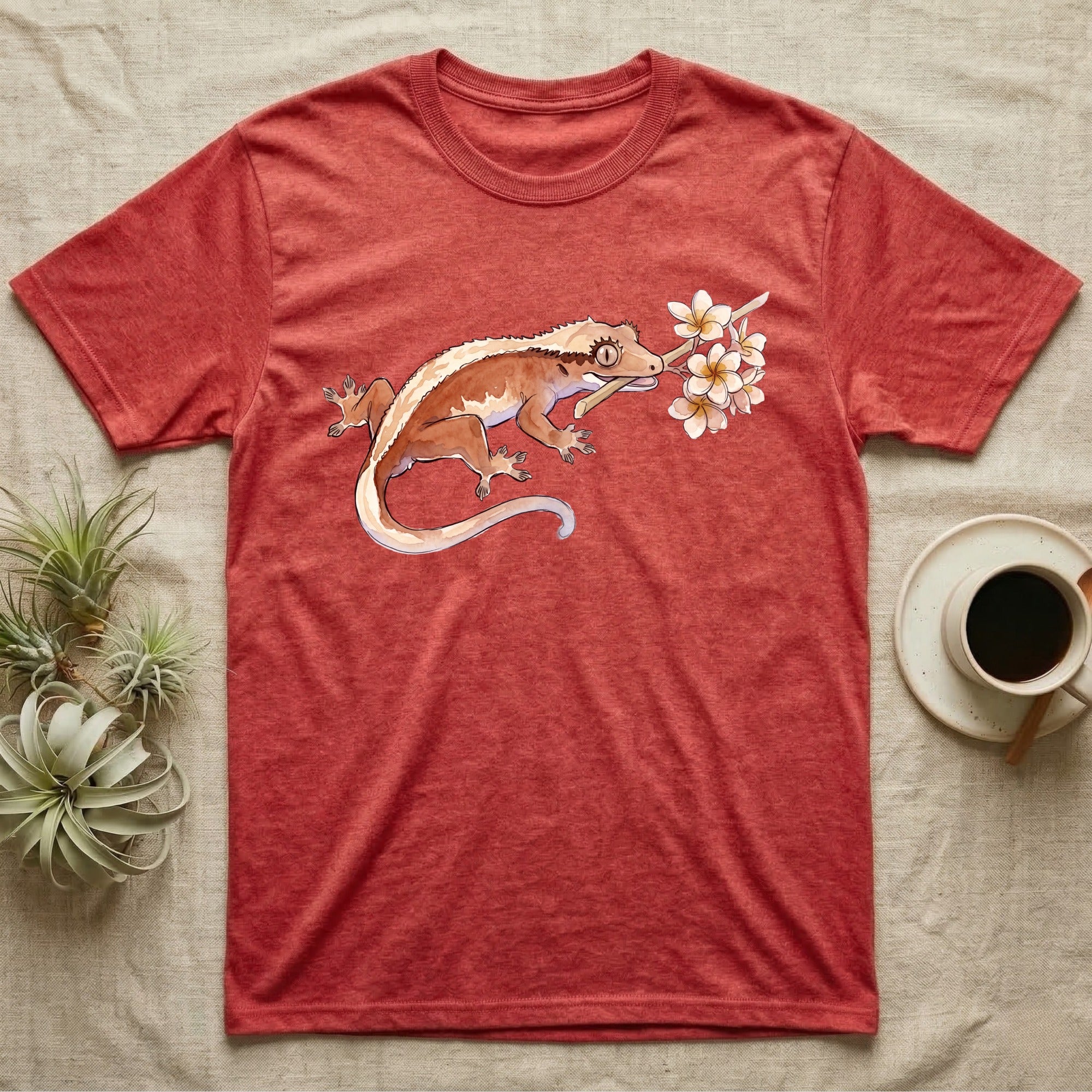 Crested Gecko Blossom T-Shirt in Heather Red — Watercolor illustration of a rust-brown crested gecko holding a frangipani blossom sprig, on a dark grey t-shirt.