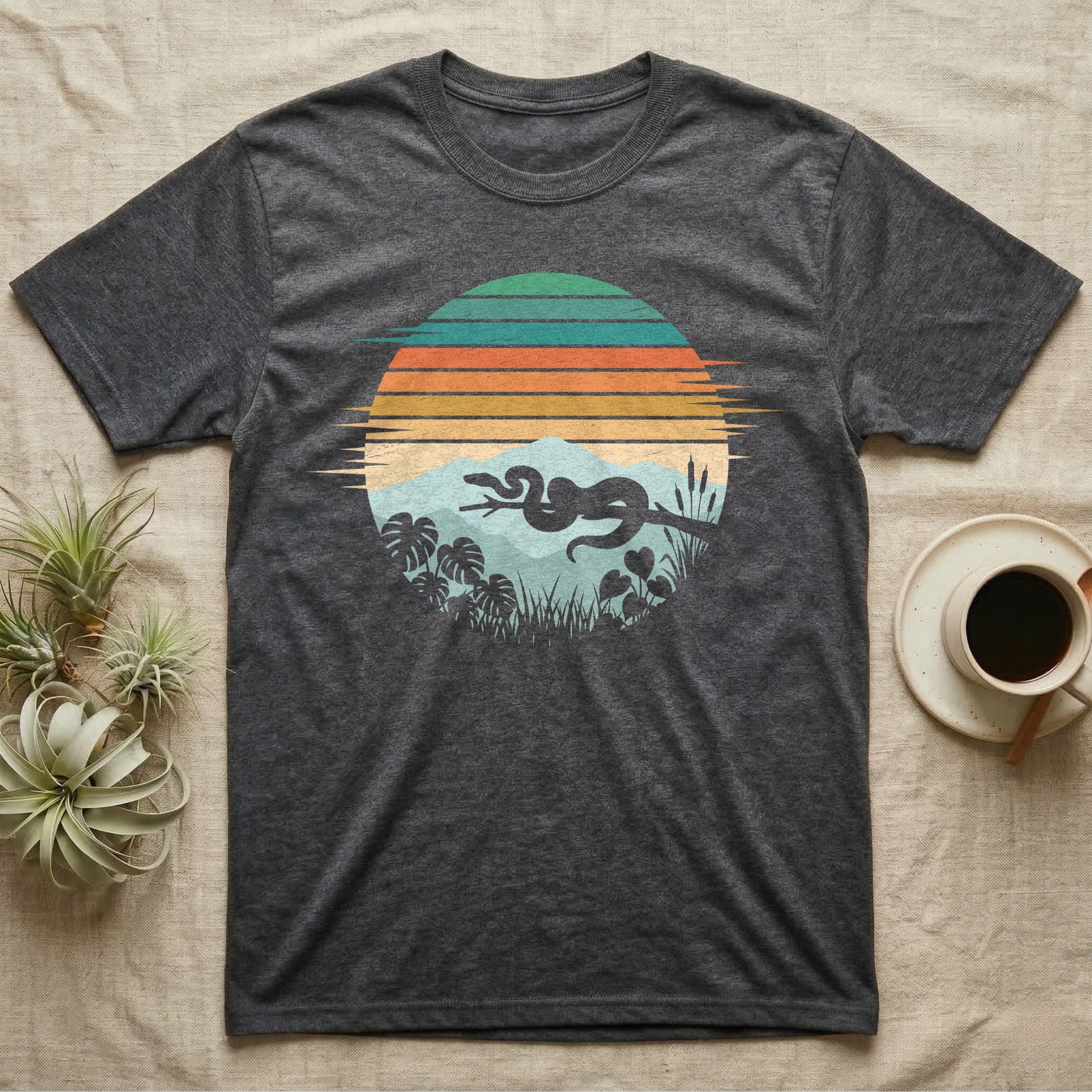 Ball Python Retro Sunset T-Shirt in Dark Heather — Ball python silhouette draped over a branch inside a retro striped sunset disc with monstera leaves on a tee