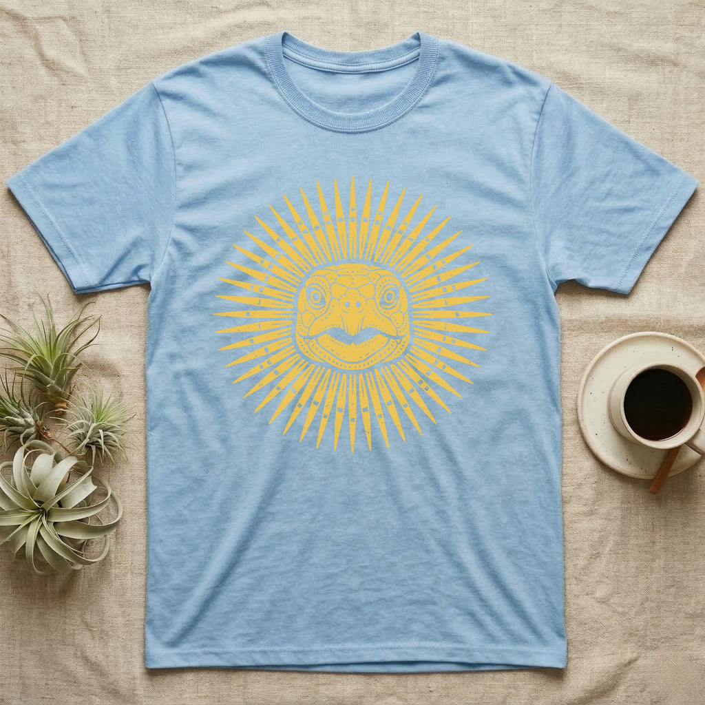 Hermann's Tortoise Sunburst T-Shirt in Light Blue — Horn-yellow woodblock Hermann's tortoise seen head-on, its shell scutes radiating outward into a sunburst medallion.
