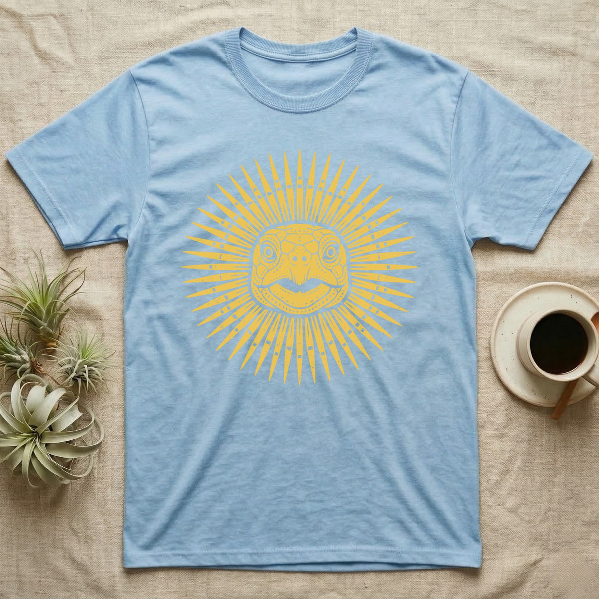 Hermann's Tortoise Sunburst T-Shirt in Light Blue — Horn-yellow woodblock Hermann's tortoise seen head-on, its shell scutes radiating outward into a sunburst medallion.