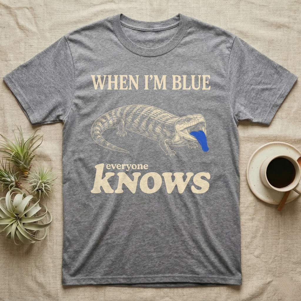 Blue-Tongue Skink Mood T-Shirt — Cream engraved blue-tongued skink on black flashing a cobalt blue tongue under the words WHEN I'M BLUE everyone KNOWS