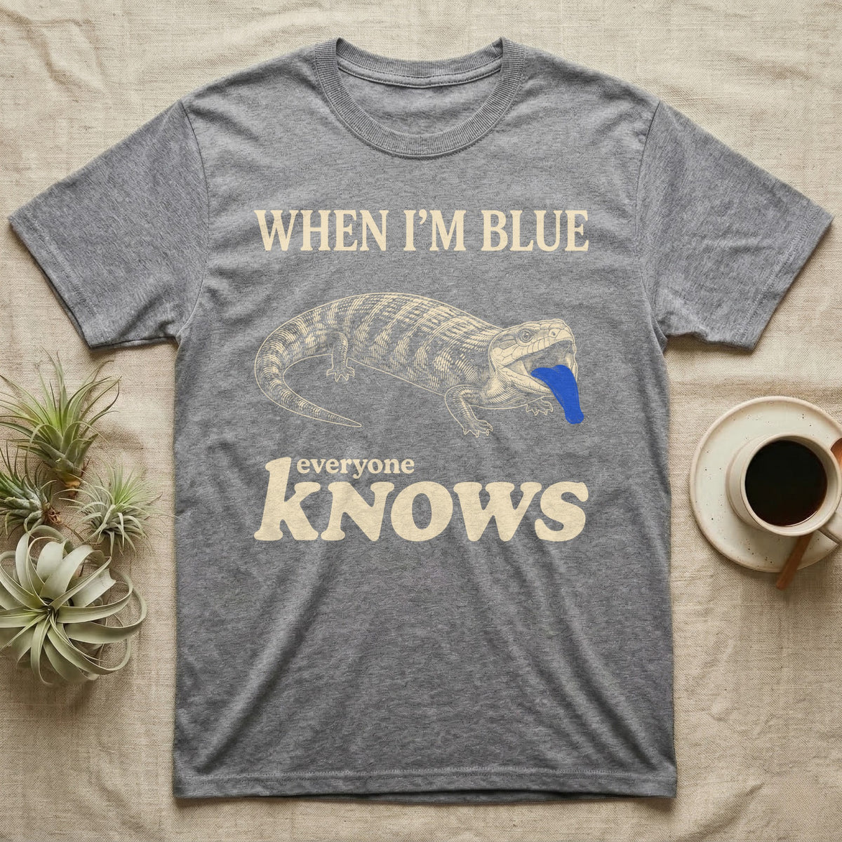 Blue-Tongue Skink Mood T-Shirt — Cream engraved blue-tongued skink on black flashing a cobalt blue tongue under the words WHEN I'M BLUE everyone KNOWS