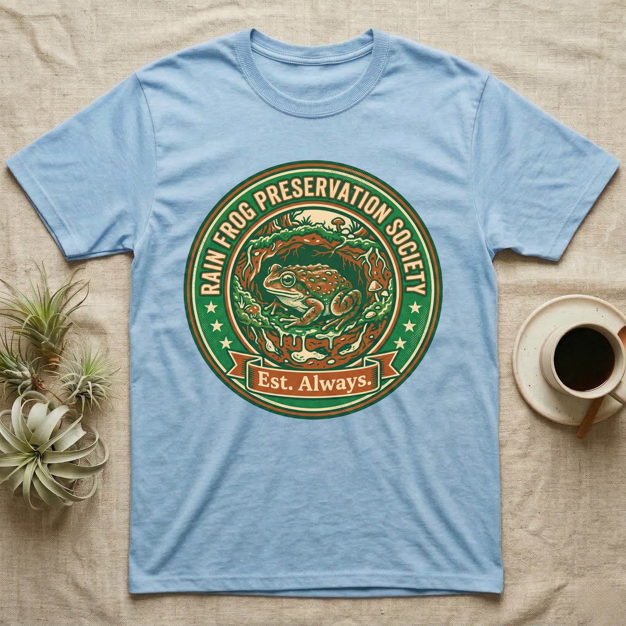 Light blue t-shirt with circular "Rain Frog Preservation Society Est. Always" logo featuring a frog.