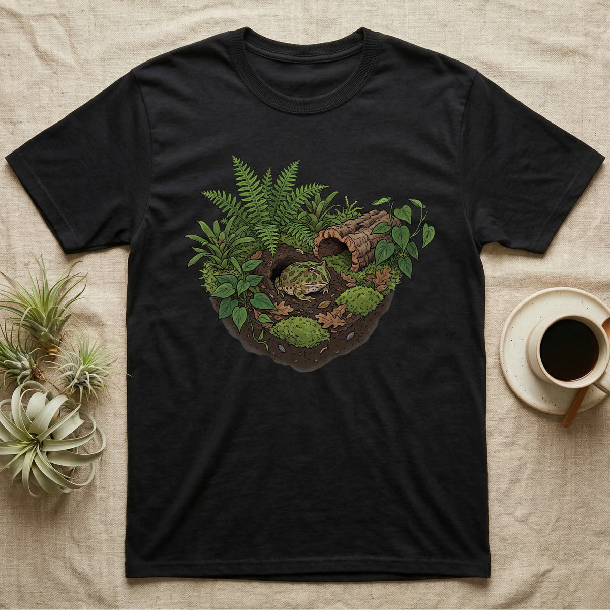 Pacman Frog Vivarium T-Shirt in Black — Botanical illustration of a pacman frog thriving in a planted bioactive vivarium beside a small empty plastic cup.