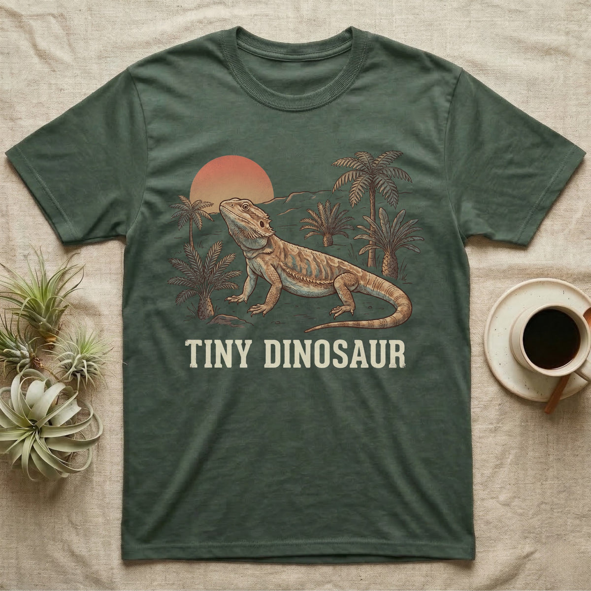 Tiny Dinosaur Bearded Dragon T-Shirt in Military Green — Retro natural-history illustration of a bearded dragon in profile in a prehistoric landscape with a distressed "Tiny Dinosaur" caption.