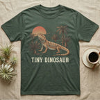 Tiny Dinosaur Bearded Dragon T-Shirt in Military Green — Retro natural-history illustration of a bearded dragon in profile in a prehistoric landscape with a distressed "Tiny Dinosaur" caption.