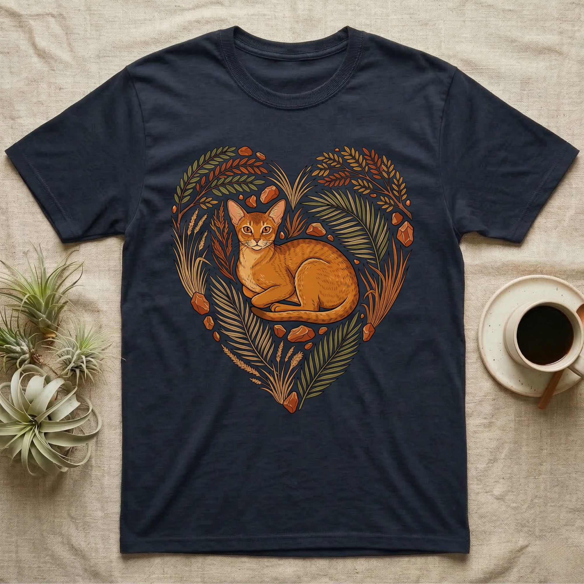 Dark t-shirt with a heart-shaped design of a cat amidst leaves and stones.
