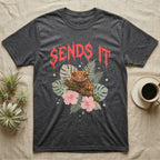 Crested Gecko Feral T-Shirt in Dark Heather — Crested gecko on a mossy branch in a pastel jungle scene under a spiky coral metal wordmark reading SENDS IT.