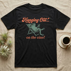 Tomato Frog Vine Vibes T-Shirt in Black — Illustrated tomato frog reclining in a beach chair with sunglasses and a cocktail, coral script reading Hanging Out On The Vine.