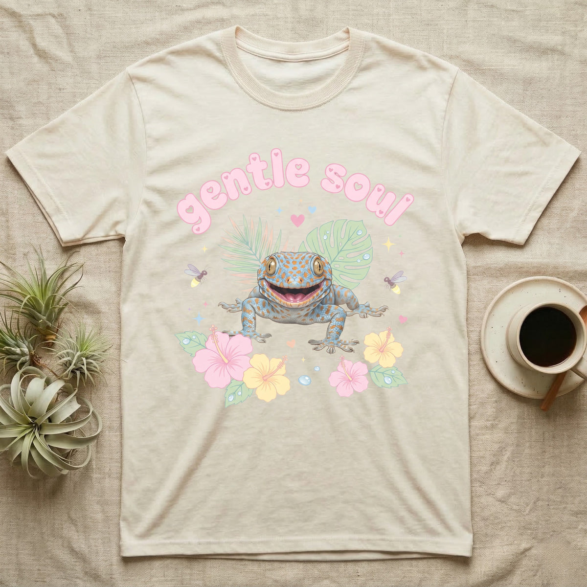 Tokay Gecko Baby T-Shirt in Natural — Blue-and-orange spotted tokay gecko among pastel leaves and hibiscus under puffy pink bubble text "gentle soul".