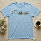 Russian Tortoise Escape Artist T-Shirt in Light Blue — Clean ink run-cycle illustration of a Russian tortoise escaping its wooden tortoise-table enclosure in three phases.
