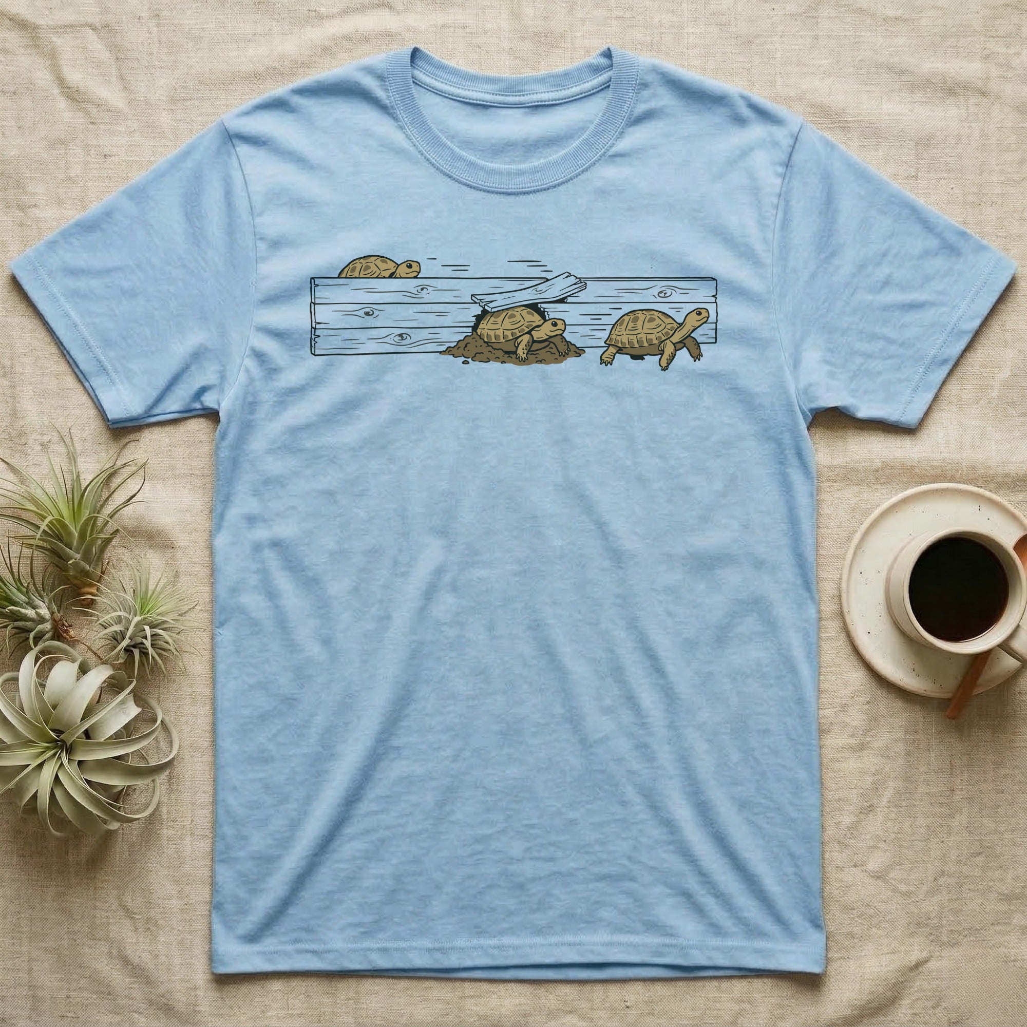 Russian Tortoise Escape Artist T-Shirt in Light Blue — Clean ink run-cycle illustration of a Russian tortoise escaping its wooden tortoise-table enclosure in three phases.